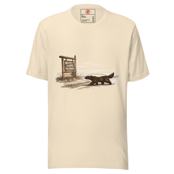 Belli Journey unisex tee in heather natural, printed with a honey badger walking a dirt road past a Welcome to Colorful Colorado sign
